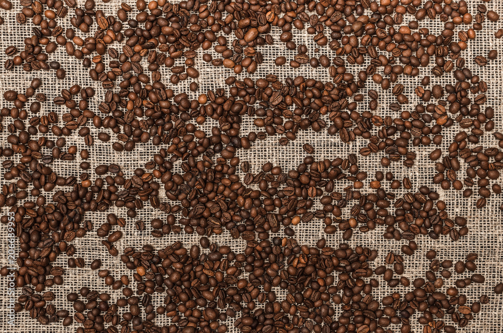 Coffee beans on burlap cloth background, top view photo.