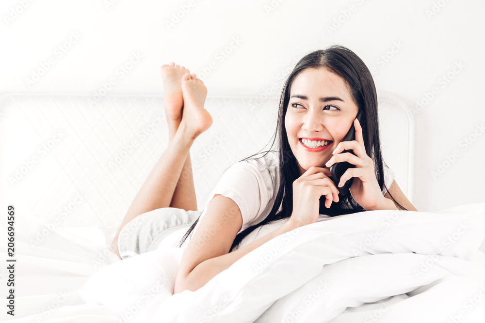 Happy woman relaxing and using smartphone on the bed at home.woman checking social apps with smartphone Happy woman relaxing and using smartphone on the bed at home.woman checking social apps with smartphone