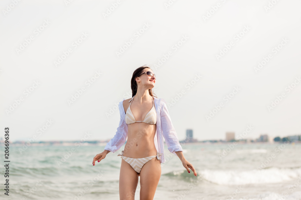 Woman in bikini walking down the beach in her summer vacation along the water