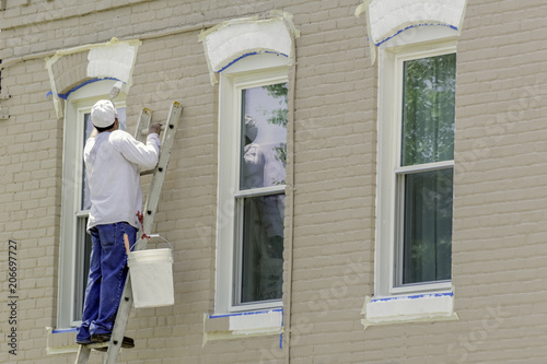 The painter paints window frames with white paint