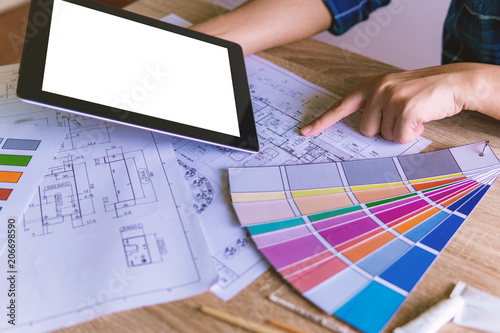 Close up hands of Interior designer designs holding tablet with empty screen that make color on blue print. engineering design at workplace concept. blank copy space.
