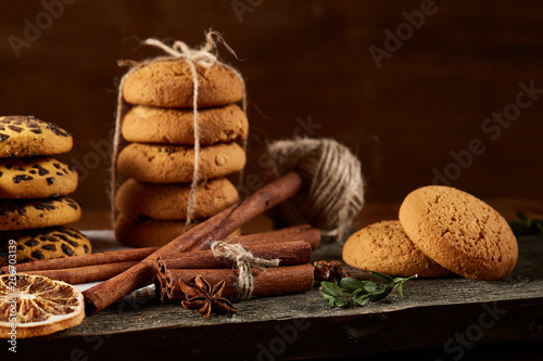 Christmas composition with pile of cookies, cinnamon and dried oranges on wooden background, close-up.