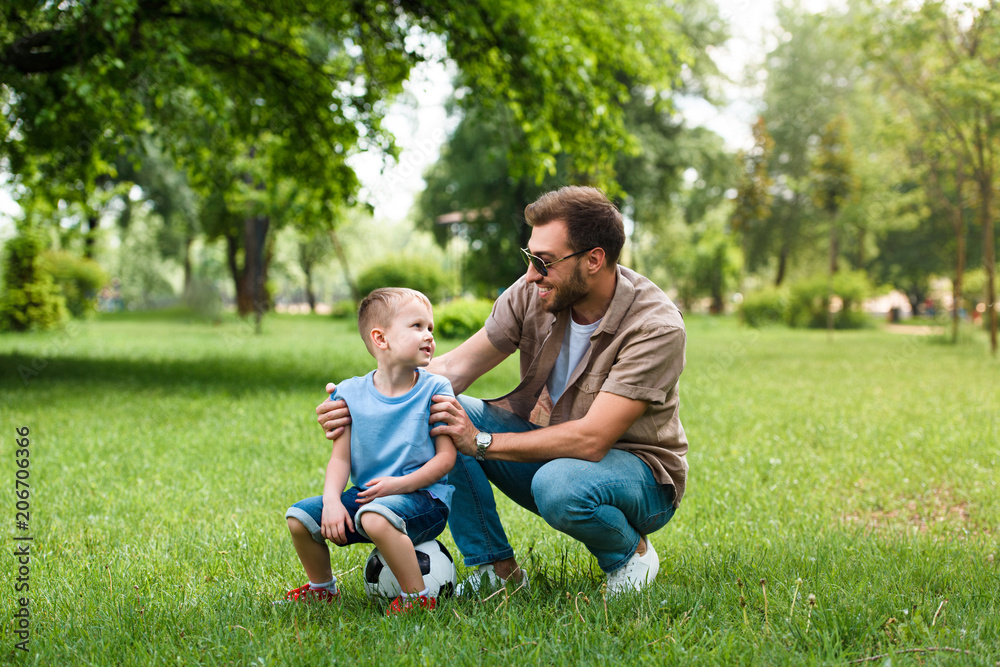 father and son looking at each other after playing football at park father and son looking at each other after playing football at park