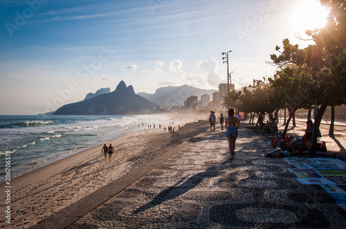 People walk on the famous sidewalk of Ipanema beach by sunset