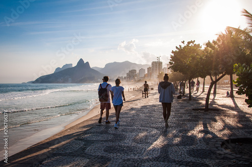 People walk on the famous sidewalk of Ipanema beach by sunset