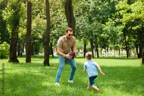 father and son playing american football together at park