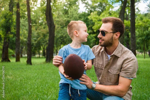 happy father and son looking at each other and holding american football ball at park © LIGHTFIELD STUDIOS