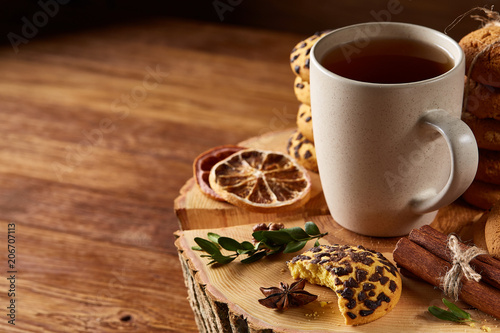 Christmas concept with a cup of hot tea, cookies and decorations on a log over wooden background, selective focus