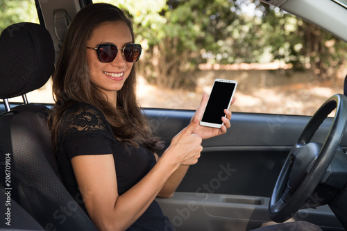 A young woman in the carh hold a smart phone with thumbs up