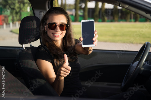 A young woman in the carh hold a smart phone with thumbs up photo