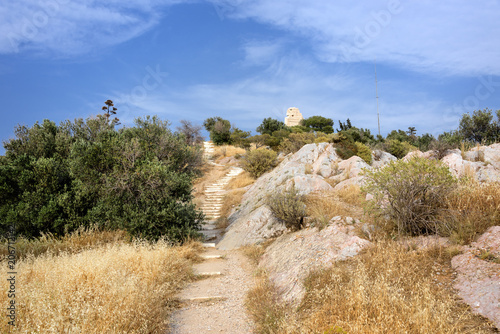 Greece, Athens: Famous Philopappu Hill in the city center of the Greek capital with Philopappu Monument, green bushes, yellow orange grass and blue sky in the background - concept nature travel beauty photo
