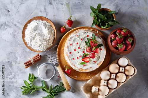 Strawberry tart covered with whipped sour cream surrounded by organic ingredients over white background, flat lay. photo