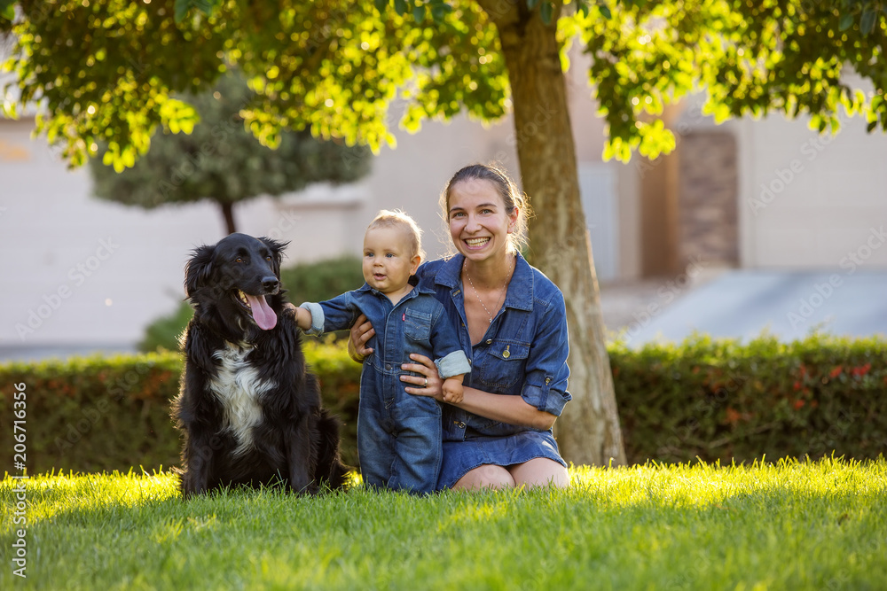 A mother with baby son and black dog in green neighborhood