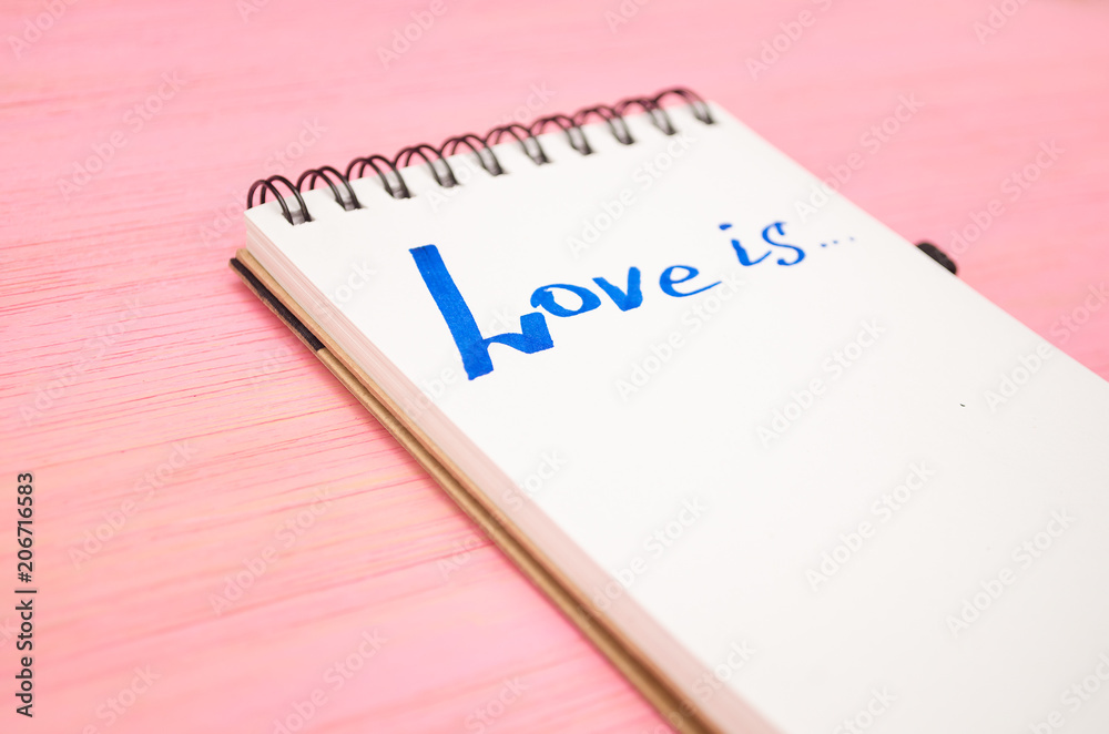 Love is inscription in notepad page on purple wooden board background. Love is inscription in notepad page on purple wooden board background.