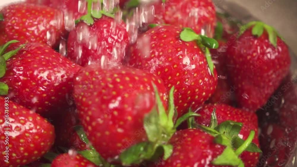 Slow motion drops of water fall on a strawberry with green tails in a metal colander Slow motion drops of water fall on a strawberry with green tails in a metal colander