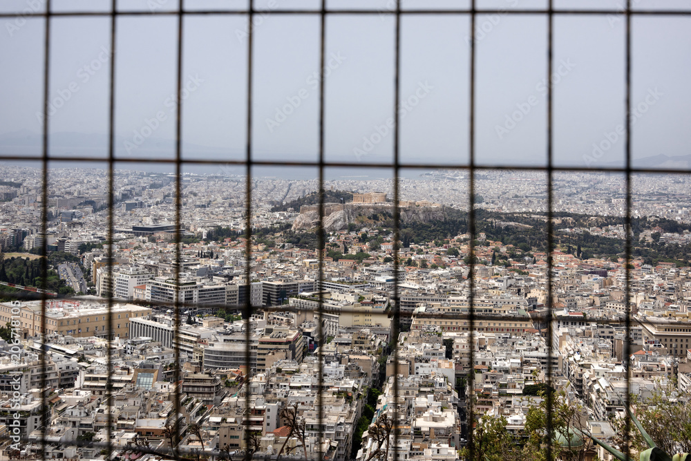 Obraz premium Greece, Athens: Skyline through fence with famous Acropolis, mass of houses, skyline, rooftops in the city center of Greek capital - concept urban development town planning structure living condition.