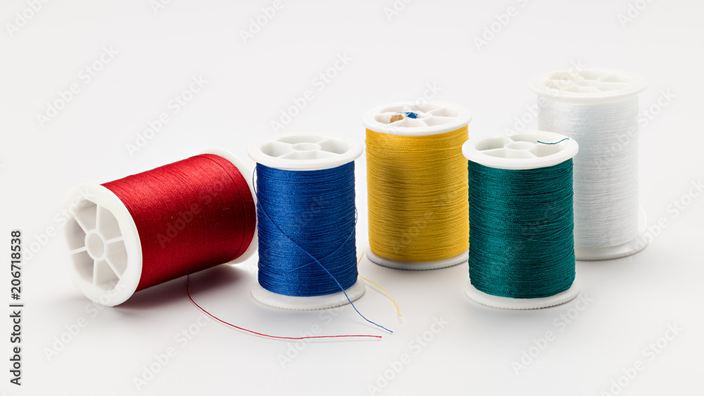 Five spools of sewing thread of different colors on a white surface Five spools of sewing thread of different colors on a white surface
