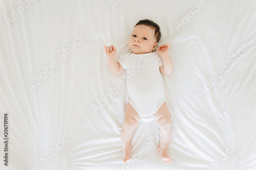 overhead view of cute newborn baby in white bodysuit lying on bed