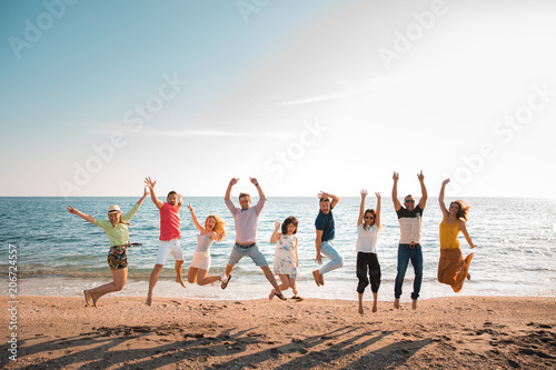 group of happy young people jumping at the beach on beautiful summer sunset. Nine person, five women and four men. Friends and holiday concept
