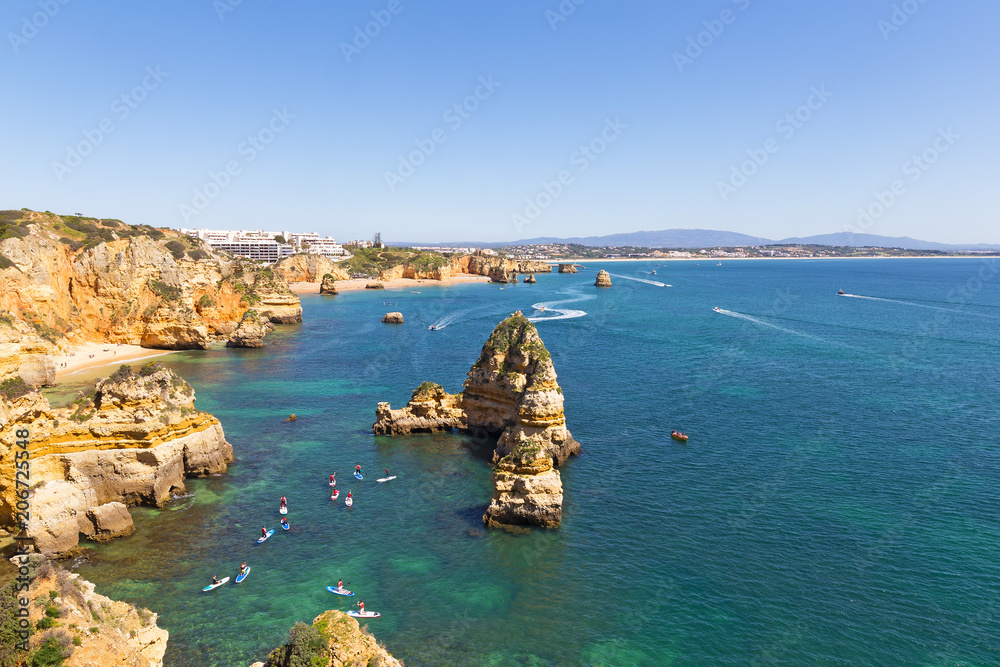 Scenic cliffs and grottos explore by tourists by kayaks and boats in Algarve, Portugal. Scenic coastline with sandy beaches and water sport activities in the morning.