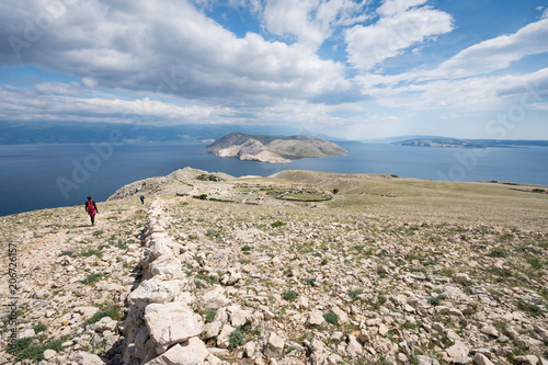 Hiker walking next to a dry-stone wall in the moon-like landscape around Baska, island of Krk, Croatia photo