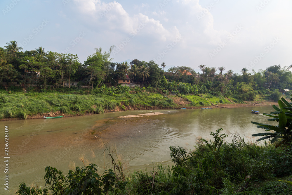 View of Nam Khan River and lush riverbank in Luang Prabang, Laos, on a sunny day. View of Nam Khan River and lush riverbank in Luang Prabang, Laos, on a sunny day.