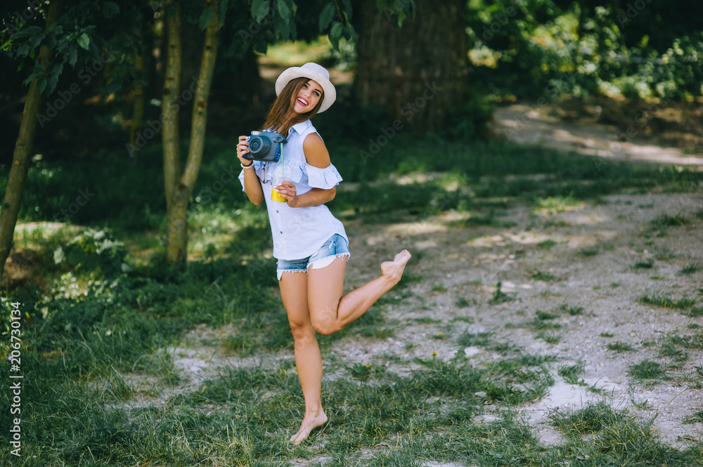 Fototapeta premium beautiful young girl in a park with a camera and juice in her hands