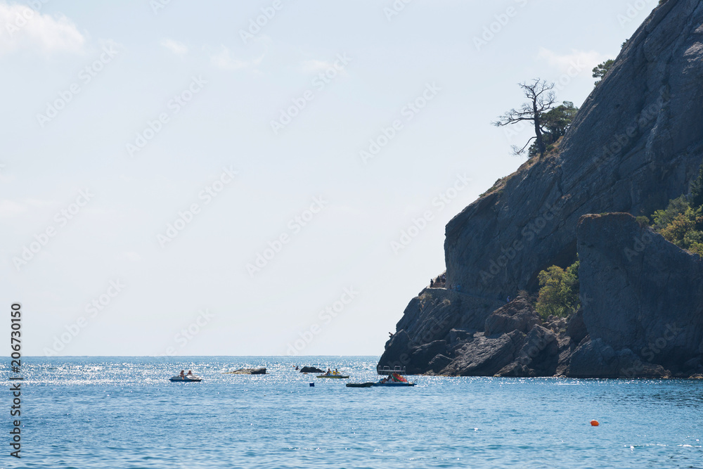 beach near the cliff. people ride on catamarans and swim, sunny day, concept of summer and rest