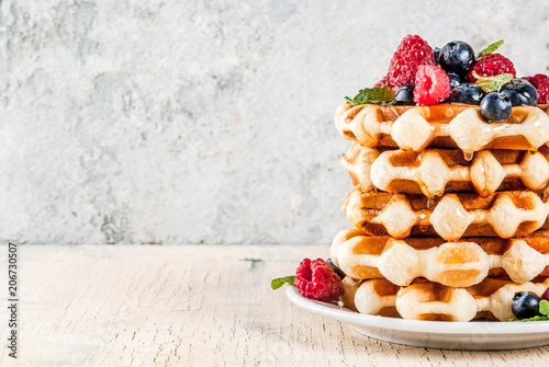 Belgian waffles with raspberries, blueberries and syrup, homemade healthy breakfast, light concrete background copy space photo