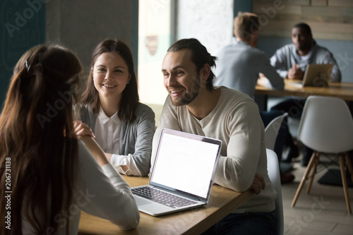 Smiling couple meeting realtor or mortgage insurance broker in cafe, financial consultant making offer to happy clients with laptop in public place, millennial friends having fun in coffee shop