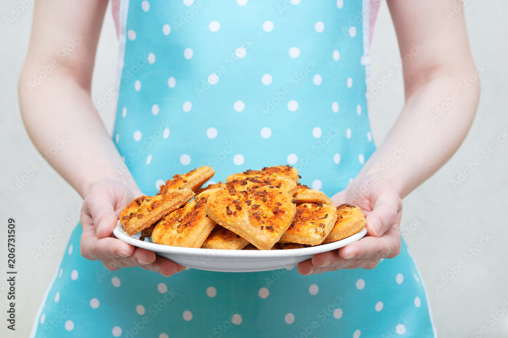 The girl in the kitchen apron holds a white plate with cookies in her hands. Close-up.