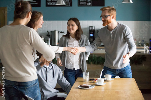 Millennial guy handshaking smiling girl introducing greeting at group meeting in cafe, happy young people get acquainted hanging together at public place, making new friends, first impression concept photo