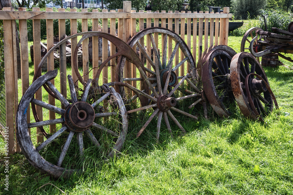 Old and broken wagon wheels against a fence Old and broken wagon wheels against a fence