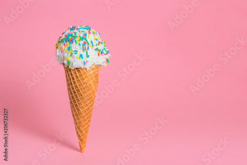 funny creative concept of close up wafer cup with ice cream and colorful sprinkles on pink background, copy space