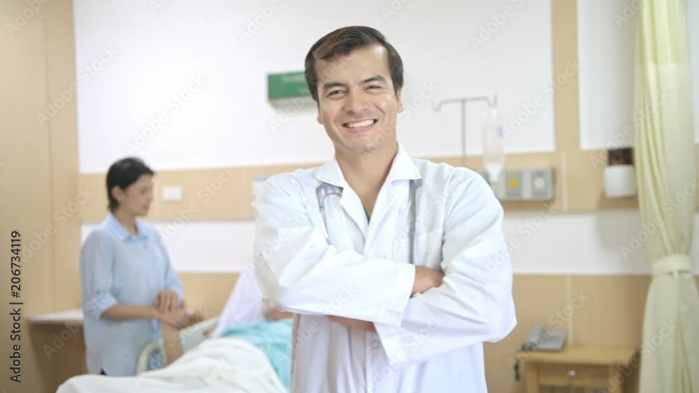 Doctor smiling portrait after successful treatment. White male doctor smile at camera with senior patient in bed looking happy with his daughter after successful treatment. Dolly shot. Doctor smiling portrait after successful treatment. White male doctor smile at camera with senior patient in bed looking happy with his daughter after successful treatment. Dolly shot.