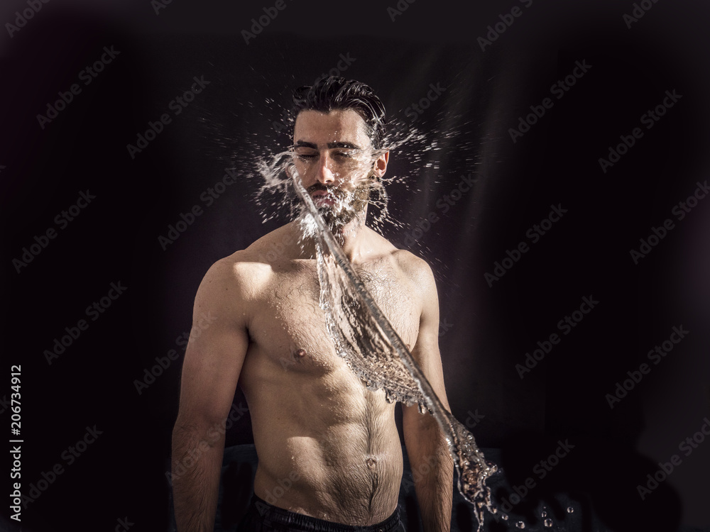 Shirtless handsome young man with water splashes on his face and chest in studio shot