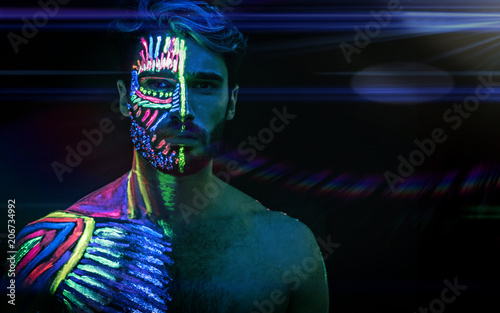 Young man painted in fluorescent paint on face and muscular torso, in  studio shot with UV light Stock Photo