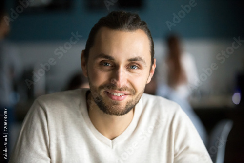 Smiling young man with attractive face head shot portrait, happy handsome millennial guy looking at camera in cafe, casual friendly businessman, entrepreneur or student posing in public place