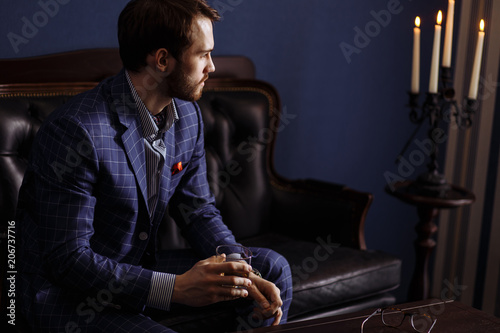 Wealthy young man sitting on the comfortable vintage sofa at mens club getting ready for meeting his businesspartners photo