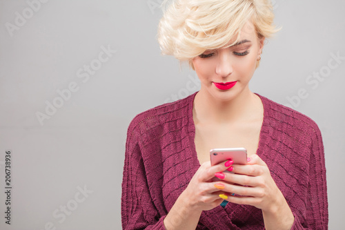 Stylysh young woman with perfect make up and trendy haicut texting or chatting on smartphone isolated on white grey background with copyspace photo