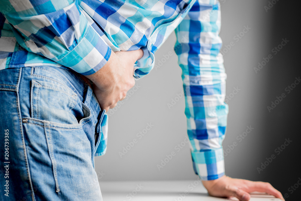 Stomach ache, abdominal ache. Isolated on gray background man stands holding his belly. Medical concept. The man has indigestion, appendicitis. Stomach flu.