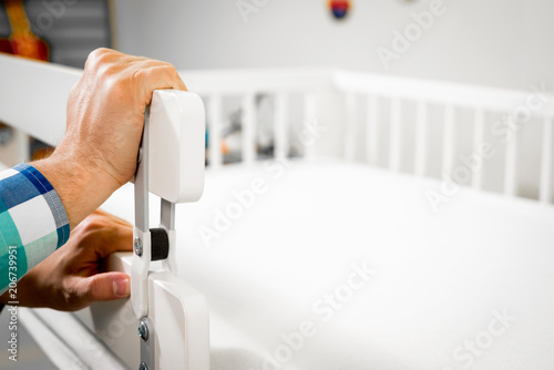 Construction of bed for children. Putting a protective railing on the bed. Role of the father in child's life. Father folds bed for a newborn child, growing up children, Concept of parenthood. photo