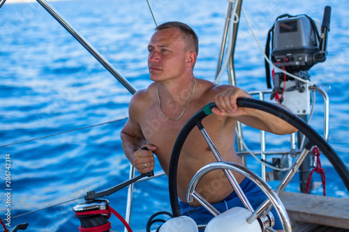 Young man with a naked torso runs a sailing yacht in the sea. © De Visu