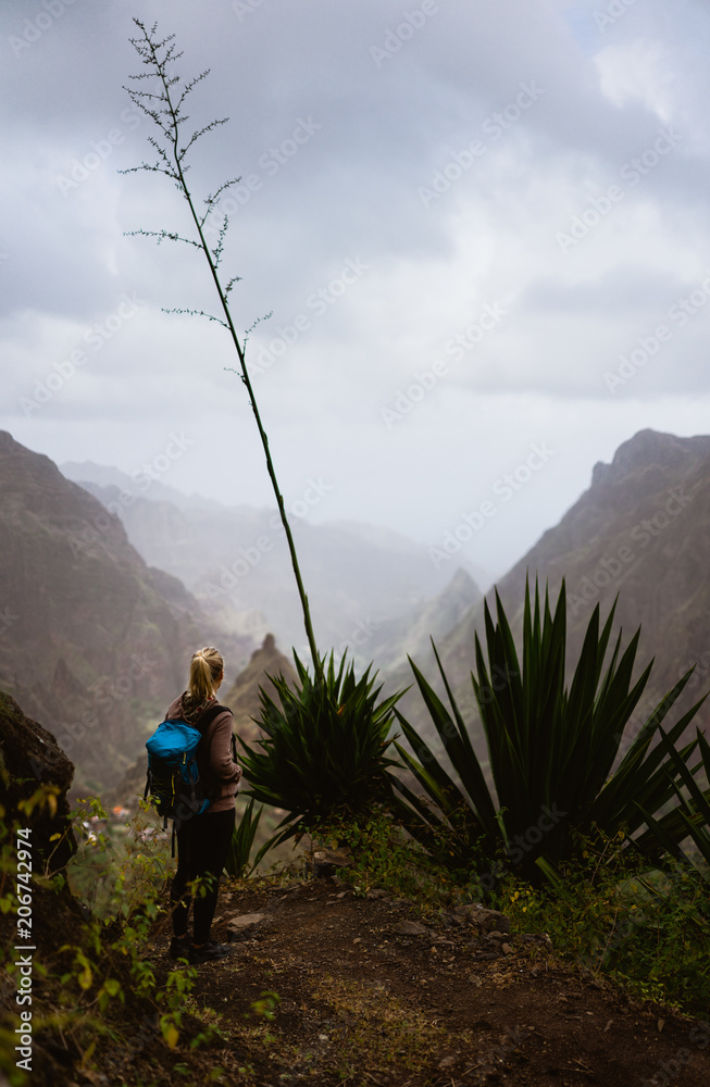 Obraz premium Female hiker in dusty mountain terrain enjoy spectacular view of sharp summits in the fog. Santo Antao Island Cape Verde