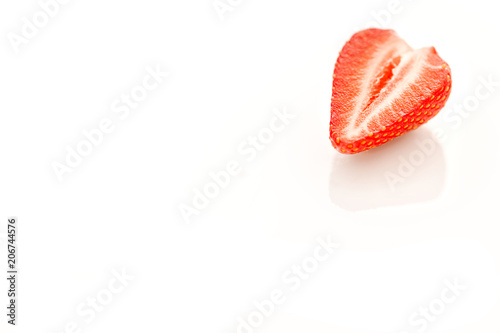 Halve of a strawberry on a reflective white background.