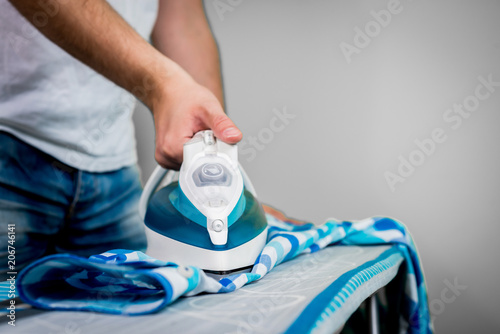 Man at home ironing clothes. A businessman ironing a shirt to work, preparing to leave the house. Man ironing shirt on ironing board with steaming blue iron.
