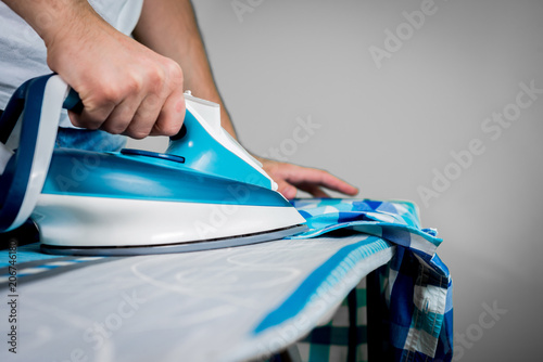 Man at home ironing clothes. A businessman ironing a shirt to work, preparing to leave the house. Man ironing shirt on ironing board with steaming blue iron.