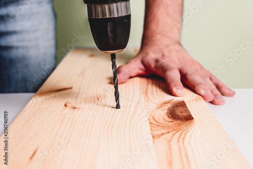 Drilling in the wooden plate. The man is holding a screwdriver or drill in hand. Drills a hole in the wall using a drill with a drill. Concept of housework, renovation at home, apartment.