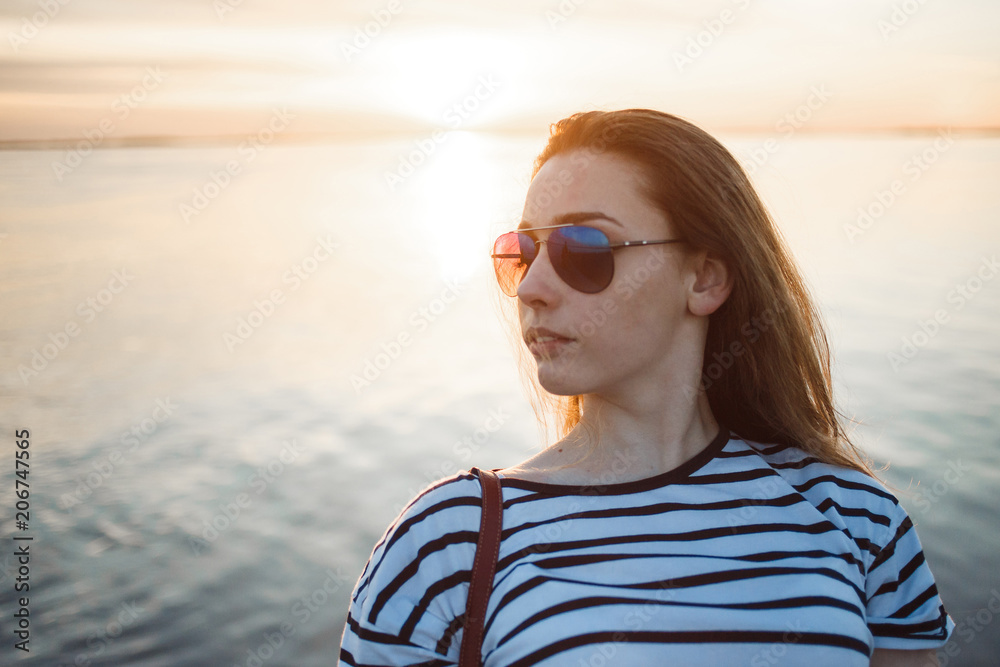 A young woman is looking at the sunset over a sea or river with beautiful soft sunny reflections in water A young woman is looking at the sunset over a sea or river with beautiful soft sunny reflections in water