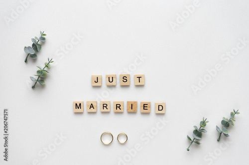 Wooden letters  spelling just married with wedding ring, oregano branches on white marble. Top view. photo